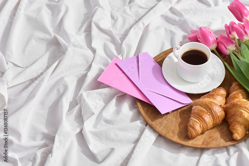 Morning celebration features a warm cup of coffee, flaky croissants, and vibrant pink tulips arranged on a wooden tray, perfect for Mother's Day breakfast in bed.