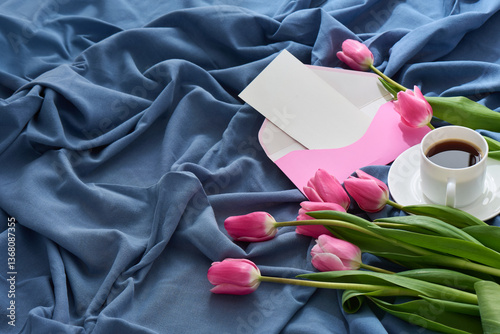 A lovely setup for Mother’s Day breakfast in bed featuring pink tulips, a coffee cup, and a greeting card on a soft, blue fabric.