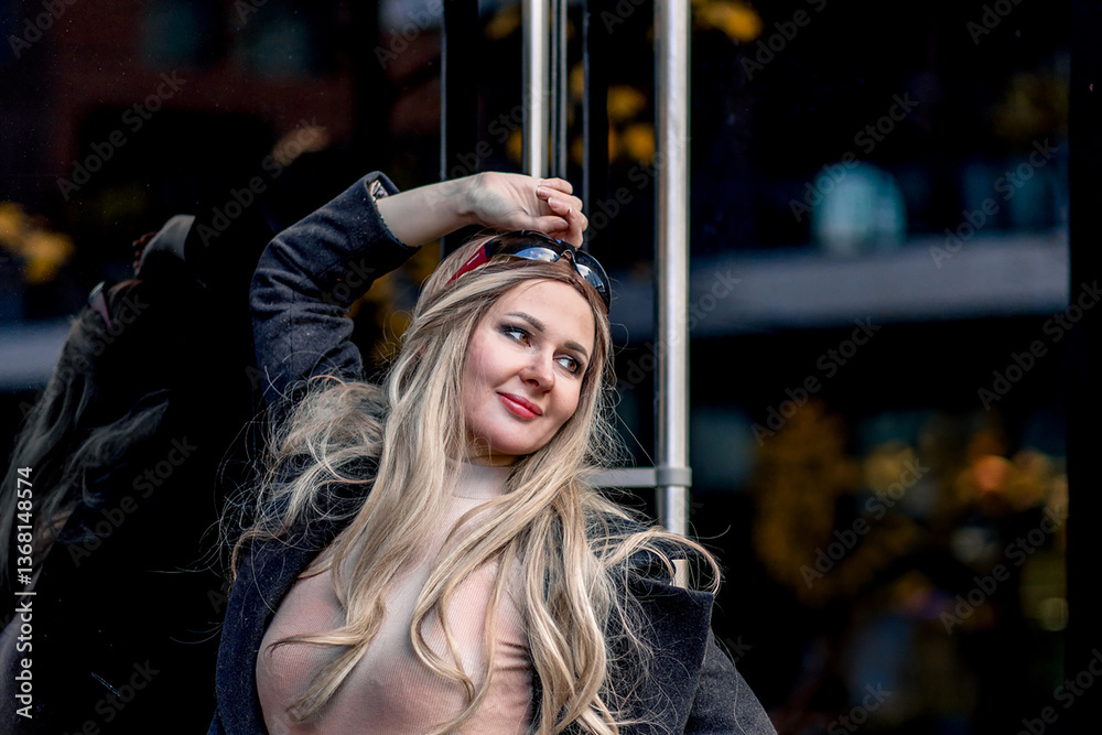 Fototapeta premium Portrait of blonde stylish woman posing near glass doors wearing black pants and coat