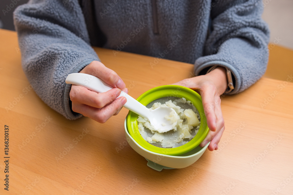 Hands preparing mashed food using baby strainer