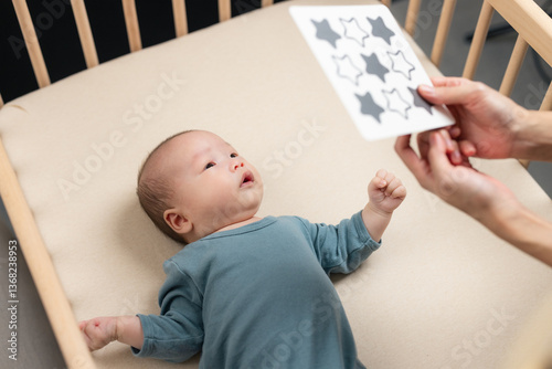 Cute baby lying in wooden crib looking at visual stimulation card