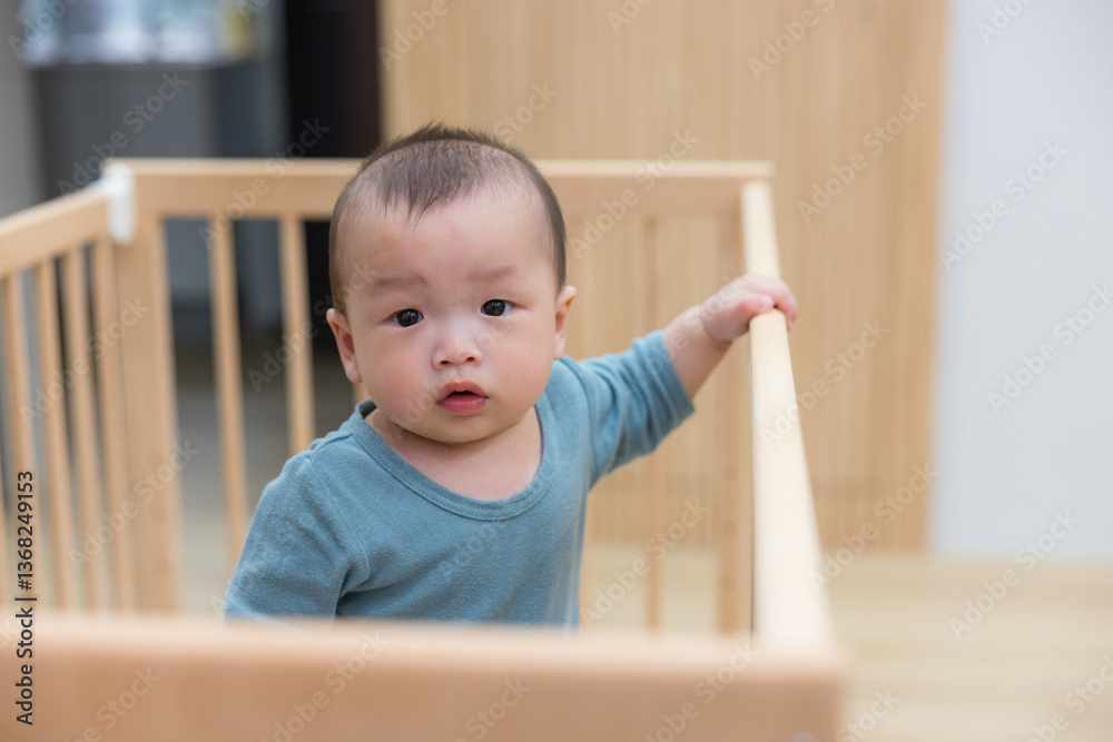 Playful infant standing in wooden baby bed