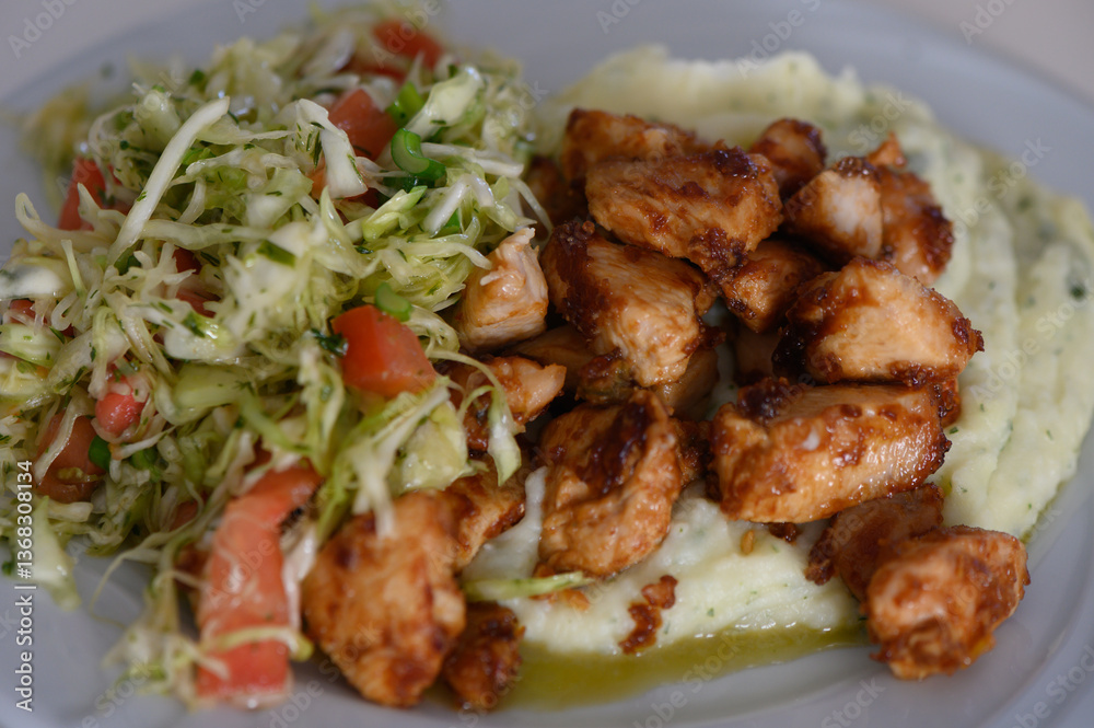 Fototapeta premium Delicious grilled chicken served on creamy mashed potatoes with fresh salad on a sunny afternoon
