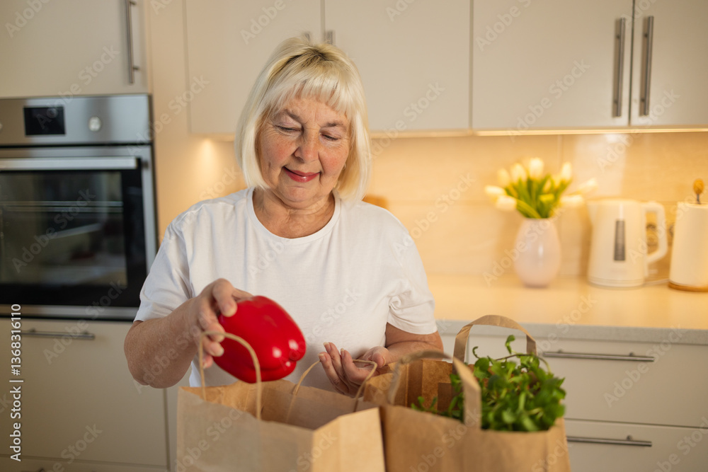 An elderly woman is unpacking groceries from paper bags in her kitchen. She places a jar of food and fresh produce on the counter, enjoying the convenience of home delivery