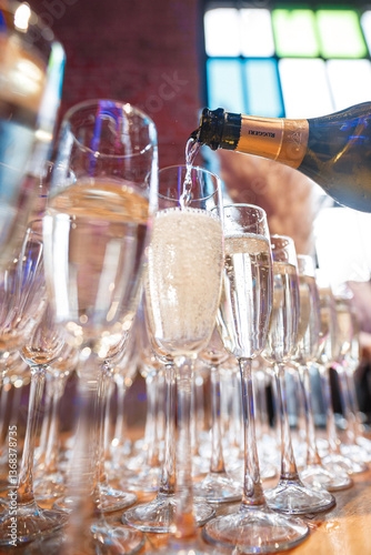 Champagne is being poured into a row of wine glasses