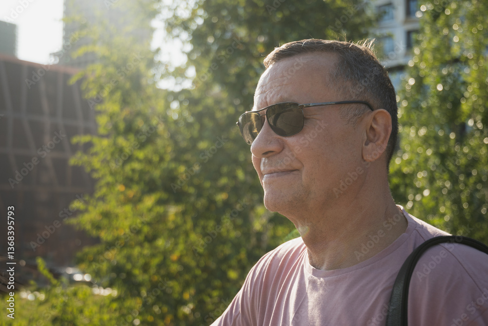 Portrait of smiling adult man wearing sunglasses and pink t-shirt at summer park. Outdoors. Close up.
