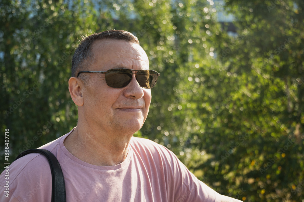 Portrait of smiling adult man wearing sunglasses and pink t-shirt at summer park. Outdoors. Close up.