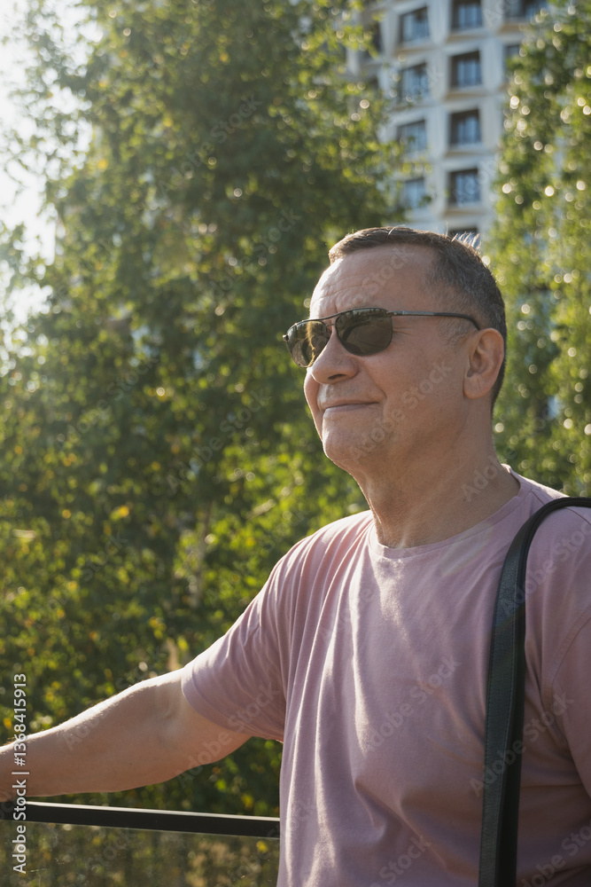 Portrait of smiling adult man wearing sunglasses and pink t-shirt at summer city public park. Outdoors. Vertical format. Close up.