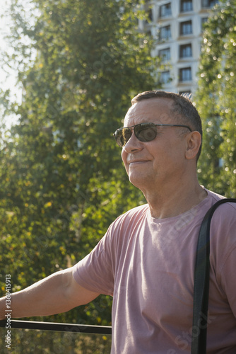 Obraz na płótnie Portrait of smiling adult man wearing sunglasses and pink t-shirt at summer city public park. Outdoors. Vertical format. Close up. w salonie