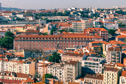 Lisbon, Portugal - Elevated cityscape view showcasing Lisbon's charming architecture. Prominent red-tiled roofs cover densely packed buildings, interspersed with green trees. Classic European view