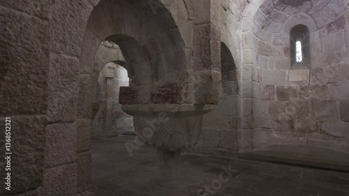 Horizontal footage moving upward from the stone floor to the vaulted ceiling inside the crypt of Leyre Monastery in Spain. The video reveals a decorated column, Romanesque arches, and a absidiole