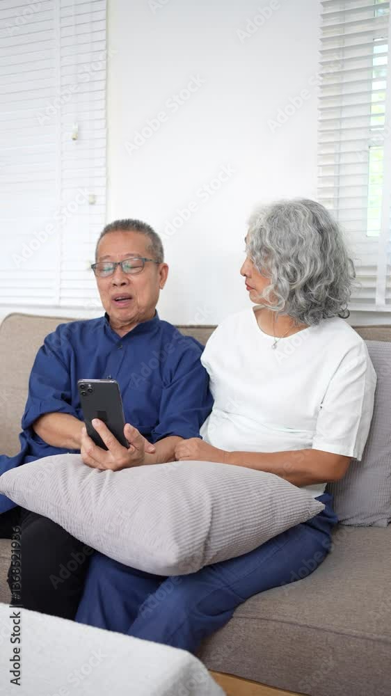 Elderly couple sitting on couch, smiling and video chatting on smartphone while enjoying cozy moment together. Elderly couple sitting on couch, smiling and video chatting on smartphone while enjoying cozy moment together.