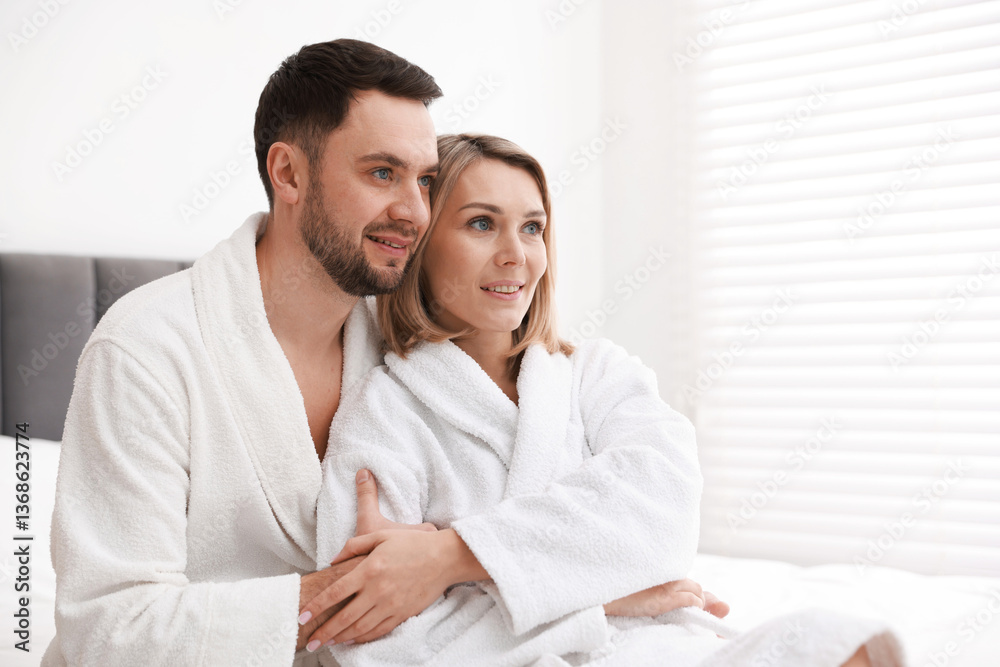 Spa. Happy couple in bathrobes sitting on bed indoors, space for text Spa. Happy couple in bathrobes sitting on bed indoors, space for text