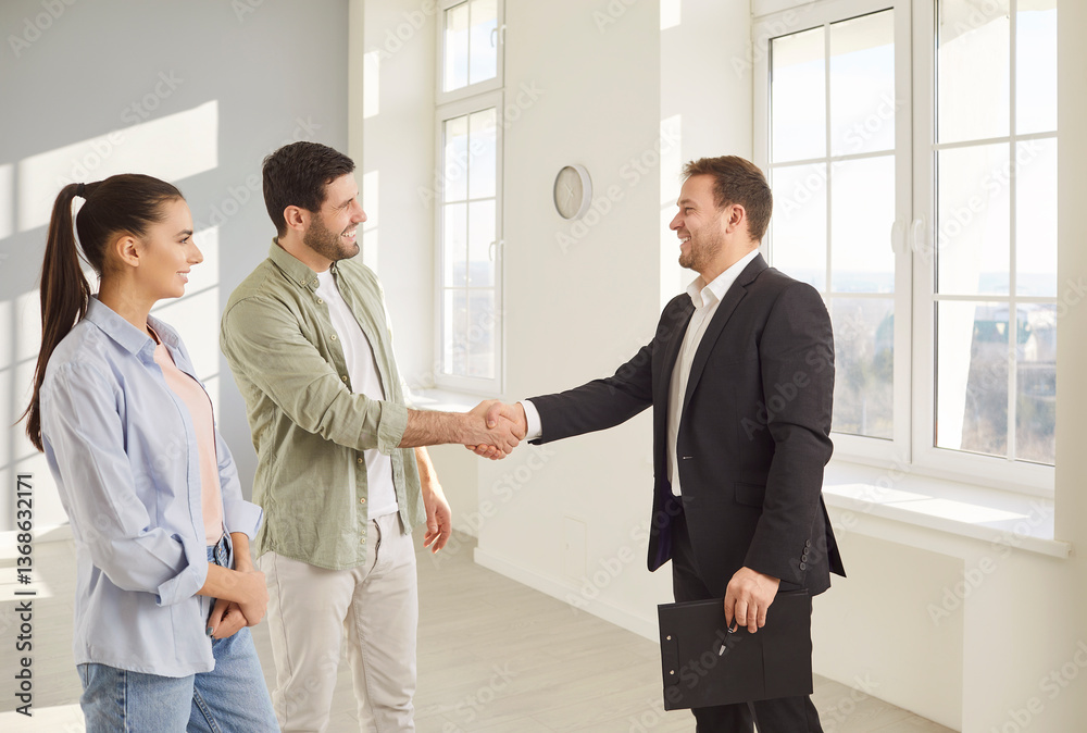 Happy smiling young couple customers shaking hands with professional man realtor making deal buying property standing in new flat. Family ready to become homeowners. Real estate market concept Happy smiling young couple customers shaking hands with professional man realtor making deal buying property standing in new flat. Family ready to become homeowners. Real estate market concept