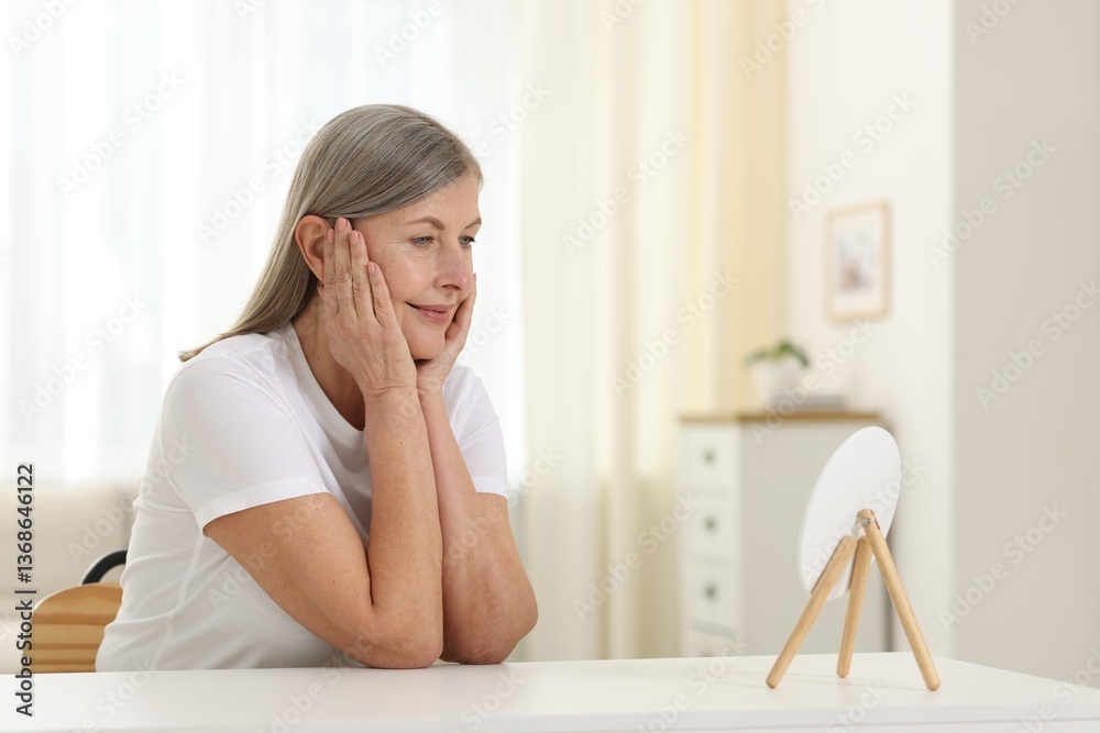 Woman with healthy skin looking at mirror at table indoors Woman with healthy skin looking at mirror at table indoors
