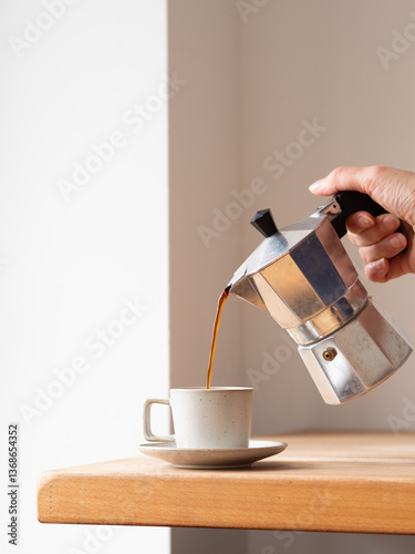 Person pouring coffee from moka pot into cup on wooden table