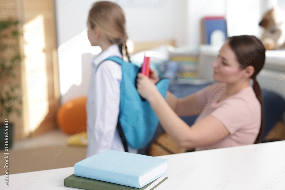 Fototapeta premium Mother helping her daughter packing backpack for school at home, focus on books