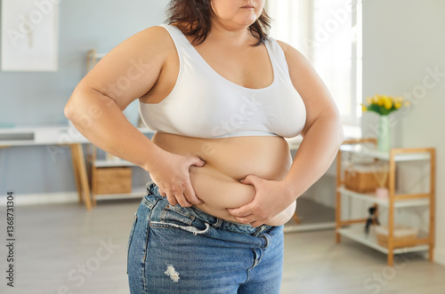 Cropped image of unrecognizable overweight young woman grabbing skin on her fat belly having health problems trying to loose weight suffers from obesity needs to have balanced diet photo