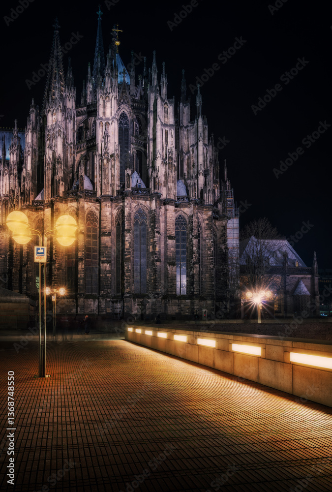 Fototapeta premium In the stillness of late evening, Cologne Cathedral comes alive in a unique way, bathed in the warm light of the street lamps illuminating its surroundings. This photo captures the majestic cathedral 