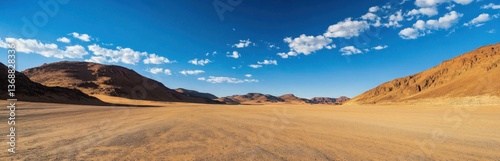 Explore a stunning desert landscape featuring expansive sandy terrain, rugged mountains, and a clear blue sky filled with fluffy white clouds. Perfect for nature lovers.