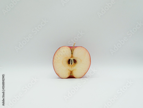 Half of a red apple, standing on a white surface, side view