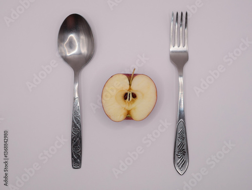 On a light background, a spoon, a fork and half an apple, top view