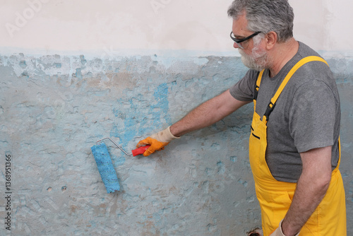 Worker using paint roller to apply adhesive primer fluid for gluing tiles