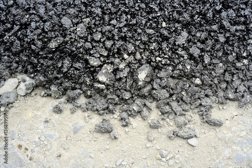 Freshly dumped asphalt on road surface
Black asphalt material spread over a pale roadbed, showing a clear contrast between the rough pavement mix and the base layer.
