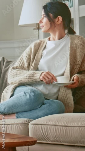 Relaxed woman drinking coffee or herbal tea and feeling carefree and refreshed while relaxing on the couch at home. Break time. Girl enjoying comfortable relaxing sitting on couch in the morning. 4K