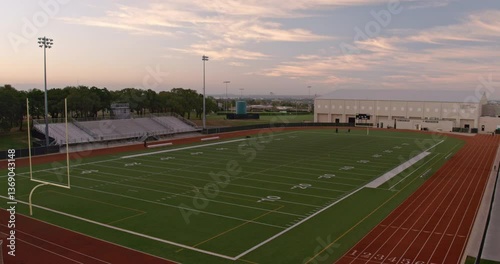 Wide aerial shot of an empty high school American football field at sunrise.