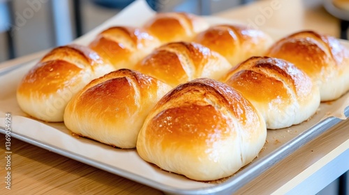 Freshly baked rolls arranged on a baking sheet.  Golden-brown, soft, and slightly glazed rolls