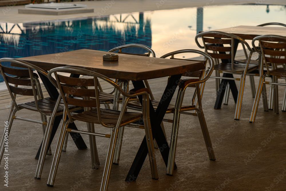 Charming outdoor dining setup by a tranquil swimming pool in the evening glow Charming outdoor dining setup by a tranquil swimming pool in the evening glow