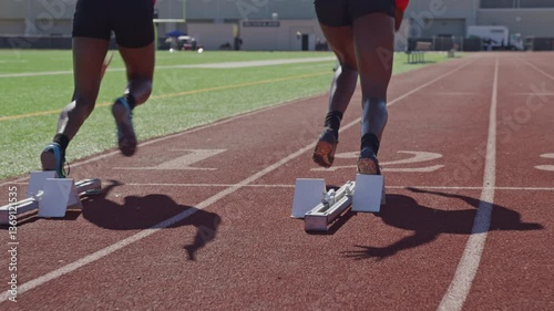 Two high school runners sprint off of starting block on a practice track