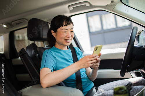 Smiling Asian woman texting on smartphone wearing sport clothes inside a car