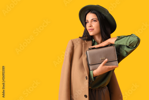 Beautiful young woman in autumn outfit with stylish bag on yellow background