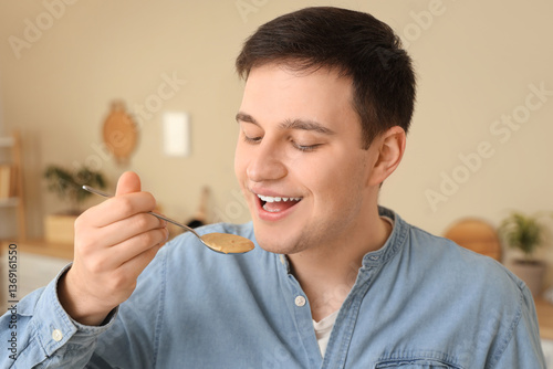 Young man holding spoon with peanut butter in kitchen, closeup