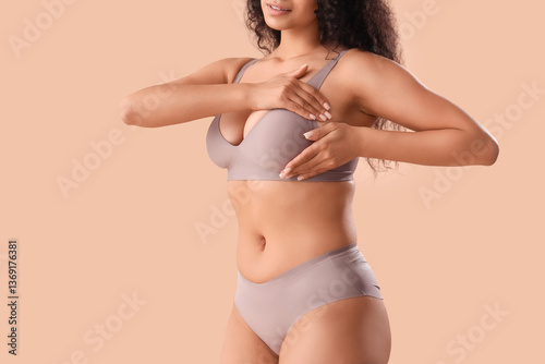 Εκτύπωση καμβά Young African-American woman in underwear checking her breast on beige background
