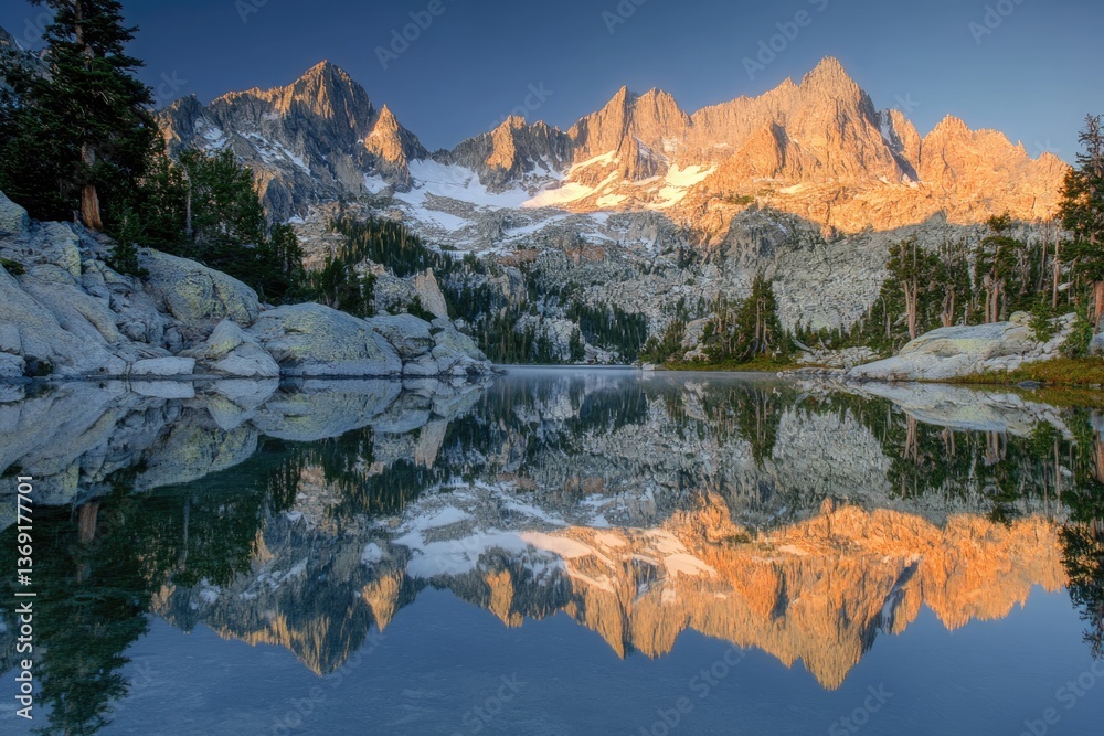 Naklejka premium Majestic mountain range reflected in a serene alpine lake at sunrise, showcasing stunning colors and tranquil beauty.