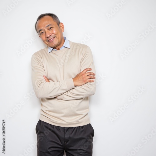 Confident Middle-Aged Asian Man Smiling Casually in a Light Sweater and Dark Pants Against a Plain Background