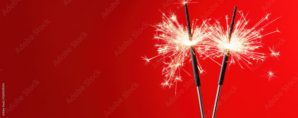 Close-up of two sparklers lit against a red background.