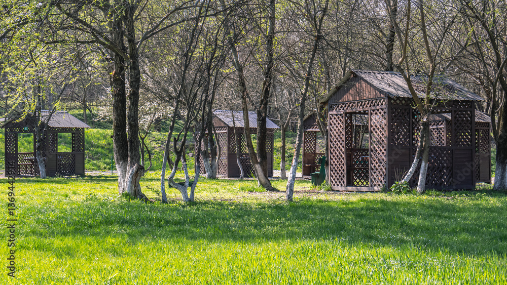 Obraz premium Wooden gazebos for relaxing in the park. A place for a family vacation in nature. A place for cooking shish kebab. Outdoor recreation in spring. Flowering trees.