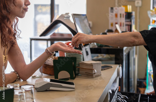 Barista handing change to female customer at coffee shop counter. Unrecognizable people