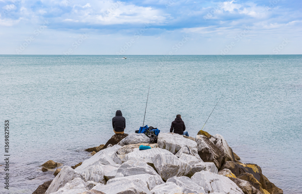 Two men fishing on the rocks of Marina di Pisa, Italy