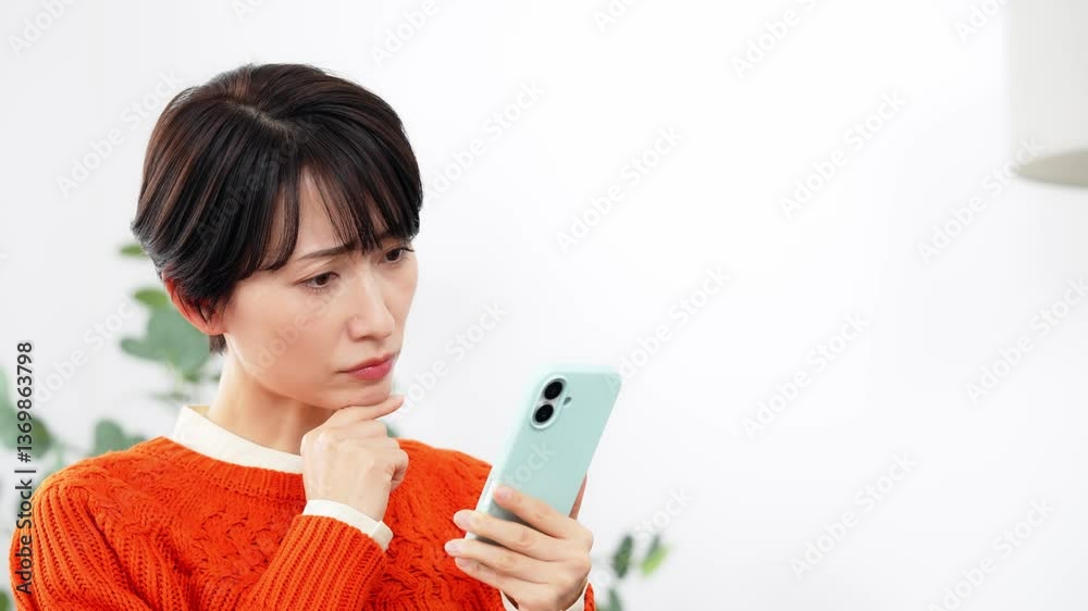 リビングルームで悩みながらスマホを見るミドル女性 リビングルームで悩みながらスマホを見るミドル女性