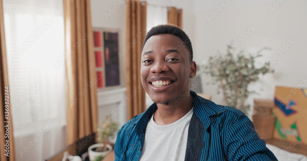 Obraz premium Smiling guy records vlog, video on social media, talking through camera with family, man shows new apartment, cardboard boxes with packed things, tells impressions