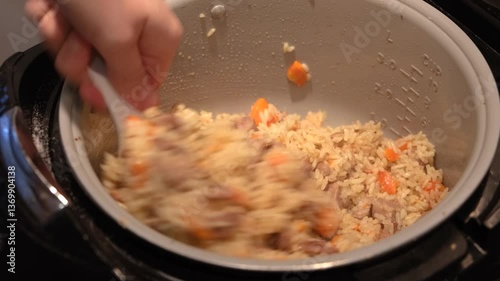 Pilaf with meat is mixed in a saucepan