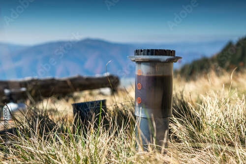 Close-up brewing coffee with an AeroPress while sitting in the mountains under a clear sky.