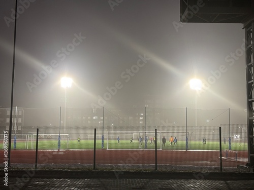 The football stadium is illuminated by lanterns during soccer practice at night during fog
