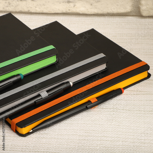 Black notebooks with colorful elastic bands and pens resting on textured surface