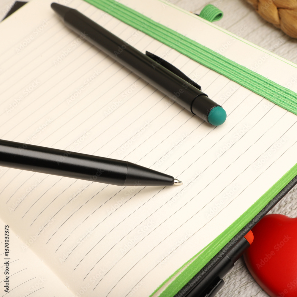Two black pens resting on an open notebook, ready for writing Two black pens resting on an open notebook, ready for writing